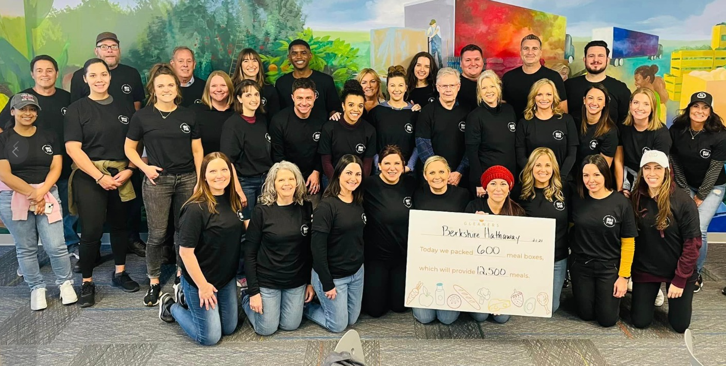 Group of people in black shirts pose in front of a colorful mural, holding a sign.
