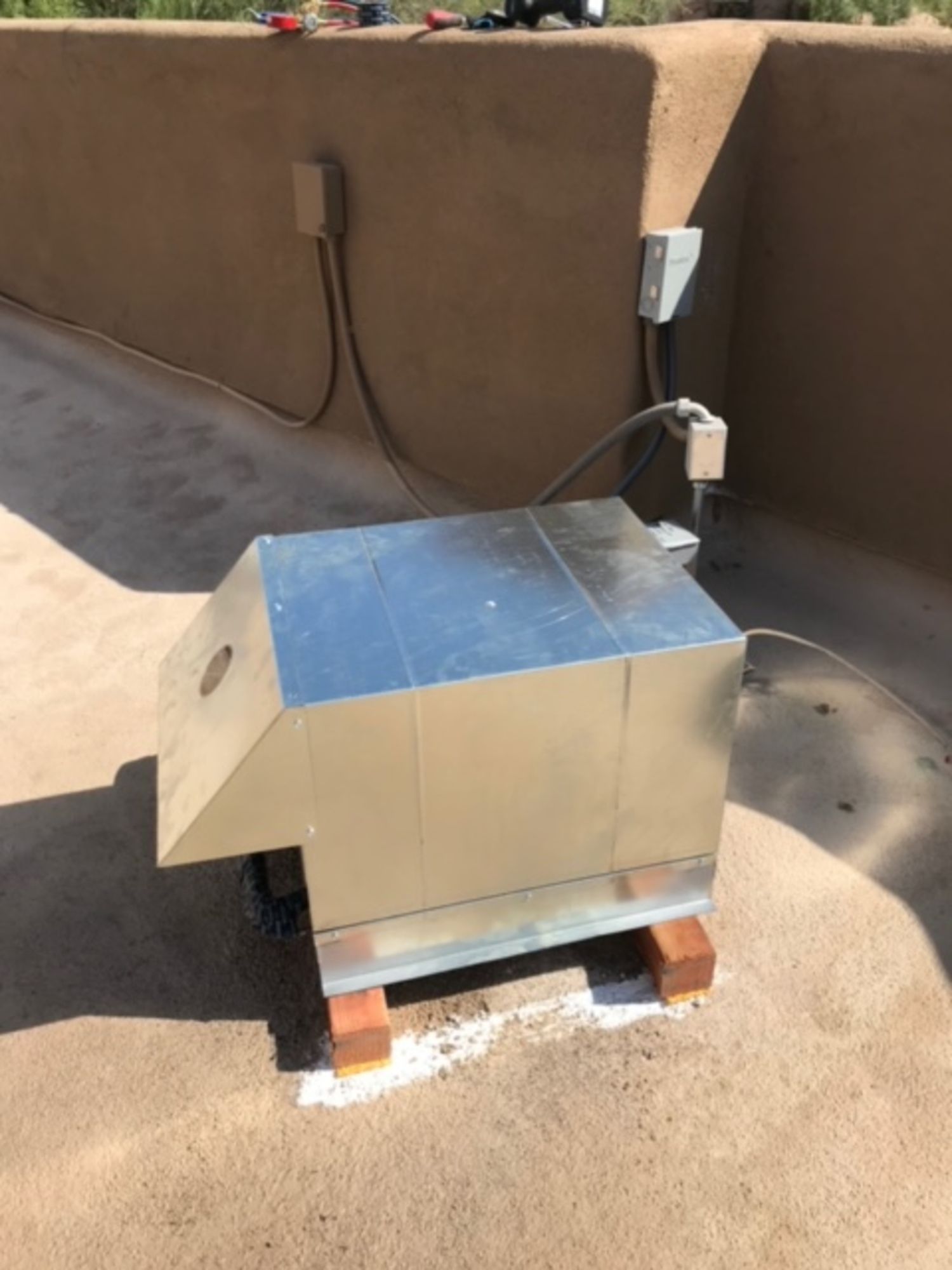 A metal box is sitting on top of a brick floor next to a wall.
