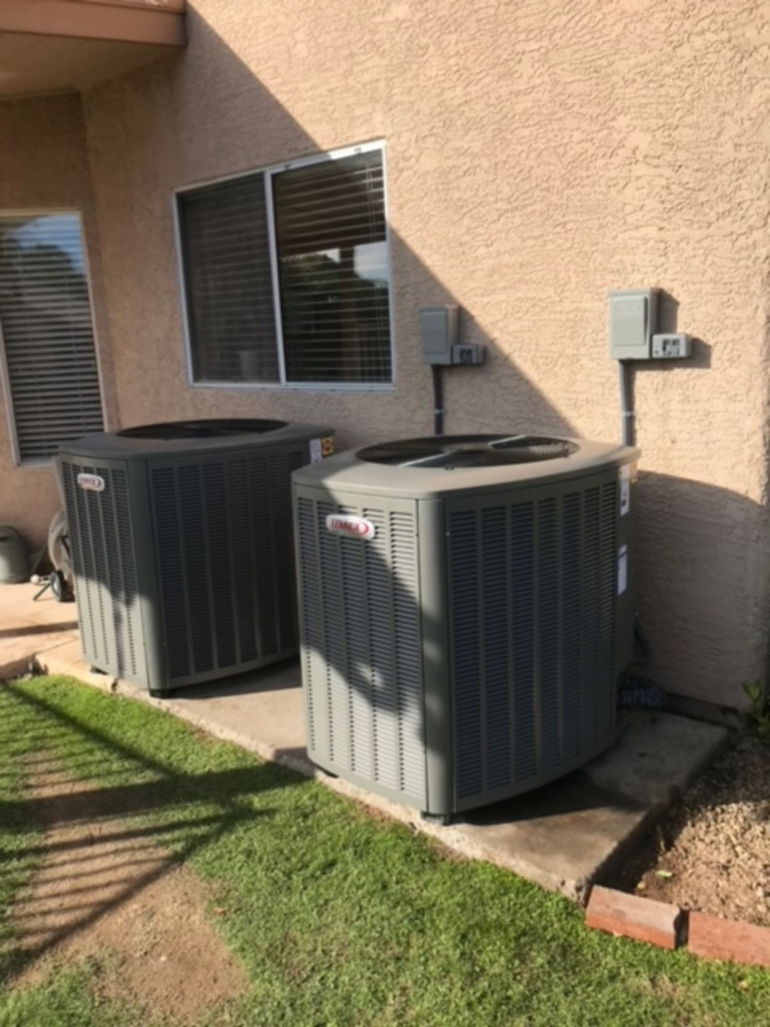 Two air conditioners are sitting on the side of a house.
