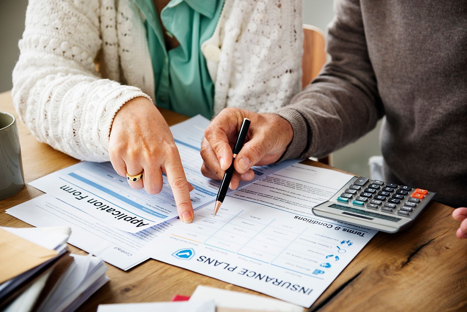 Two people review finance paperwork at a table, pointing at forms beside a calculator. Two people review finance paperwork at a table, pointing at forms beside a calculator.