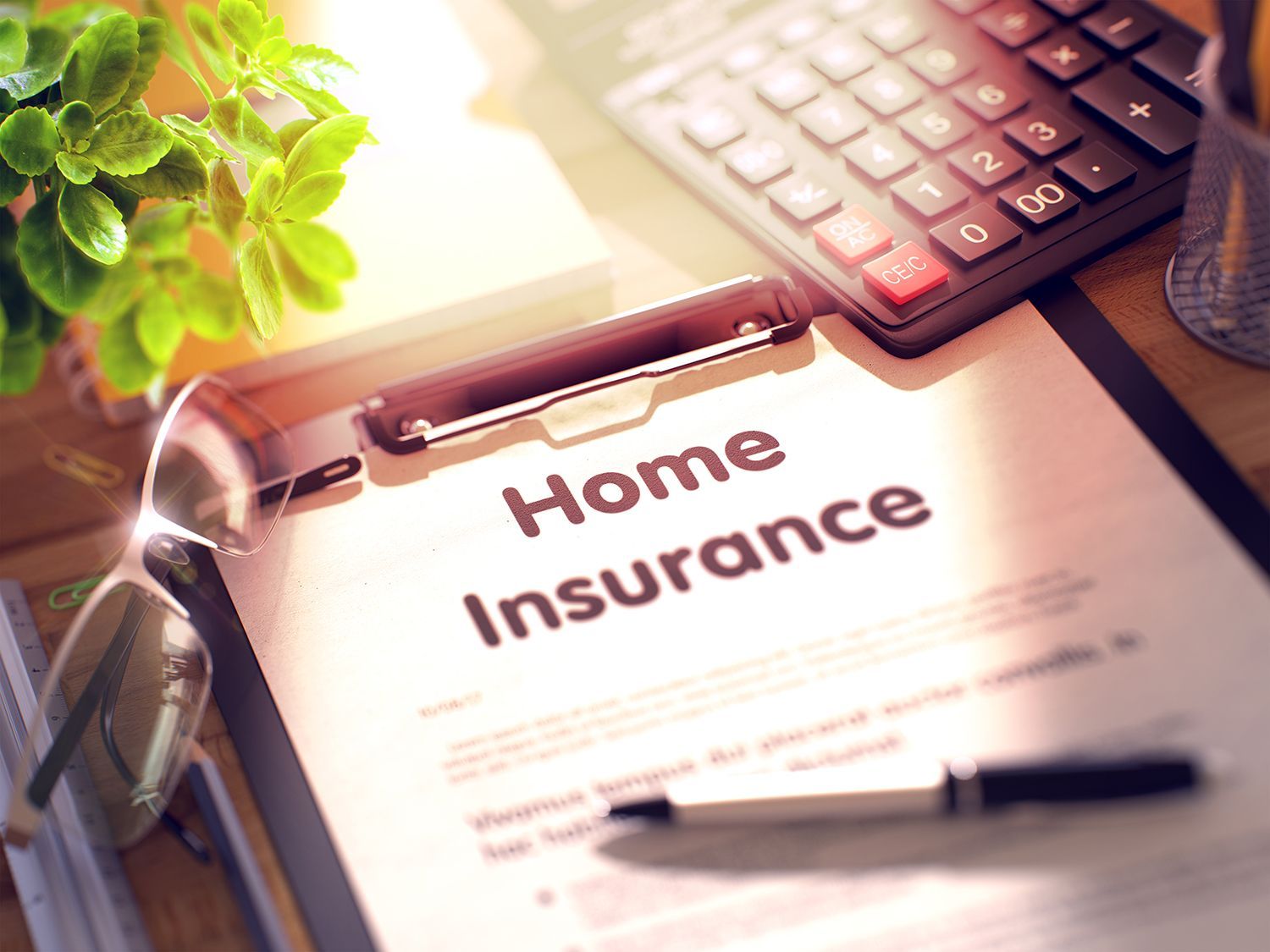 Home insurance form on a desk with a calculator, pen, glasses, and green plant nearby Home insurance form on a desk with a calculator, pen, glasses, and green plant nearby