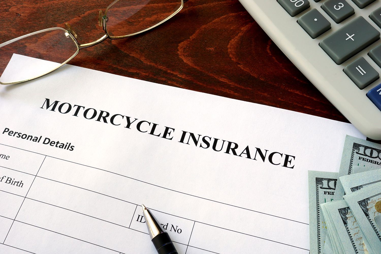Motorcycle insurance form on a desk with a pen, glasses, and calculator nearby Motorcycle insurance form on a desk with a pen, glasses, and calculator nearby