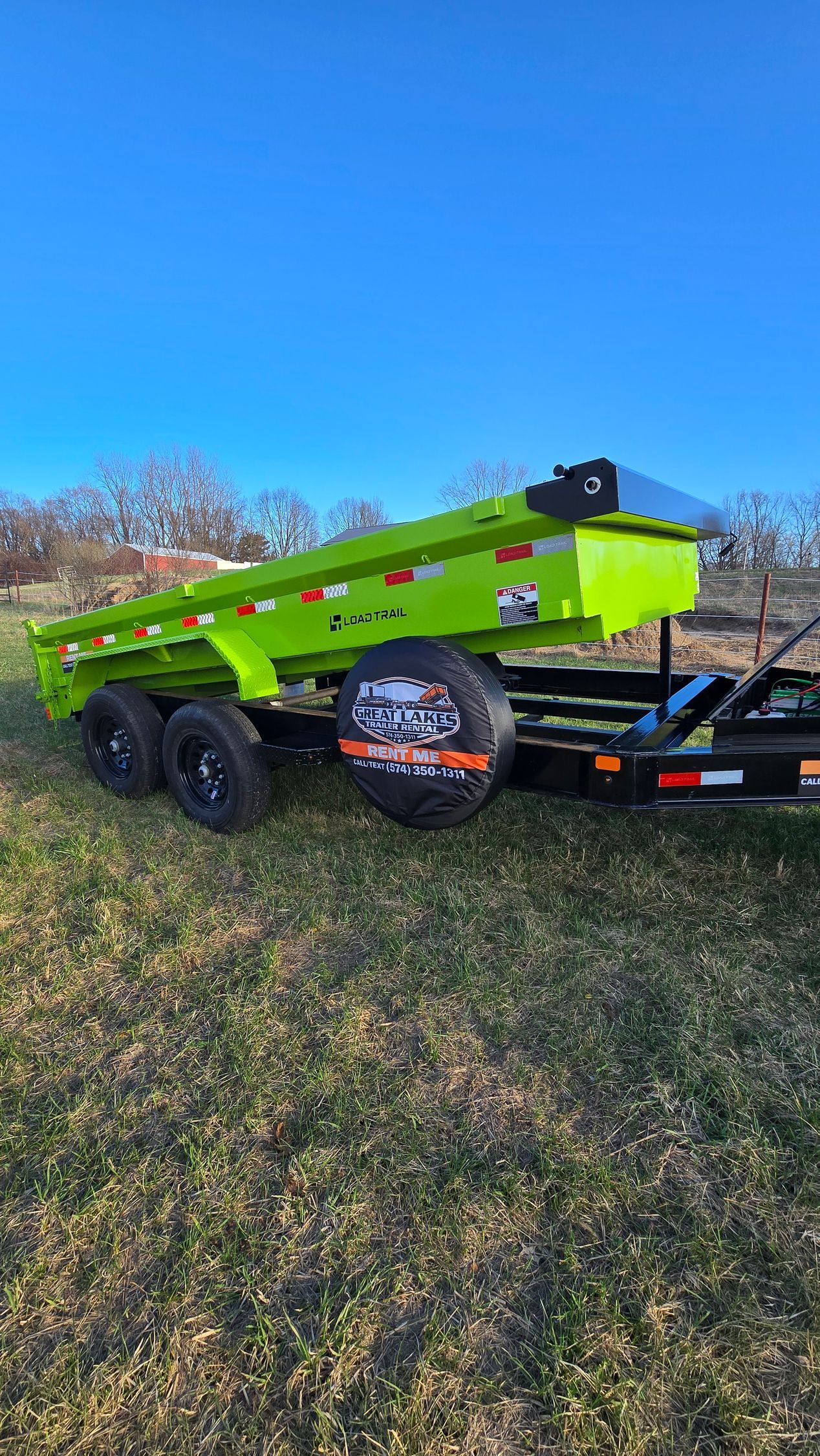 A bright lime-green dump trailer sits in a grassy field under a clear blue sky, hitched to a truck.