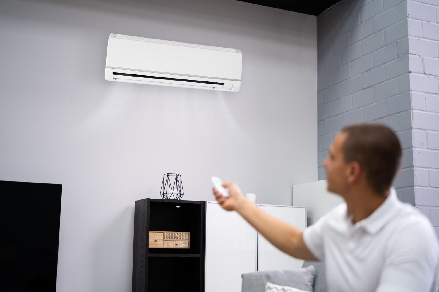 Man using remote to control wall-mounted air conditioner in a room with light gray walls.