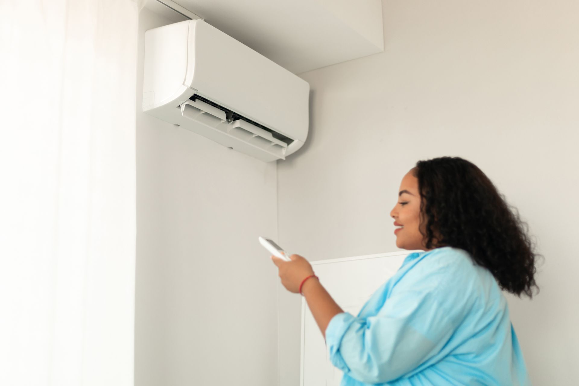 A woman is using a remote control to control an air conditioner.