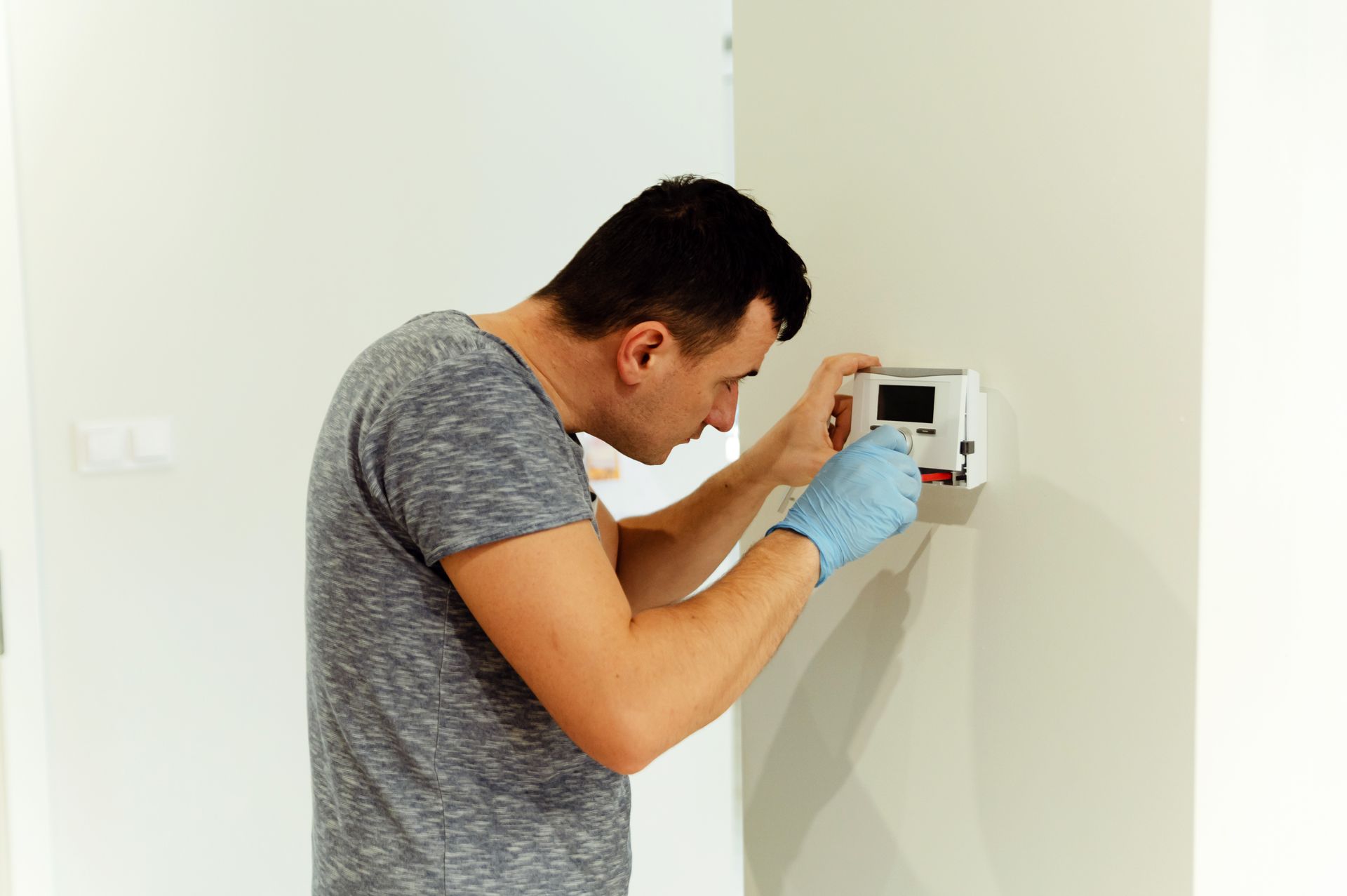 A man is installing a thermostat on a wall.