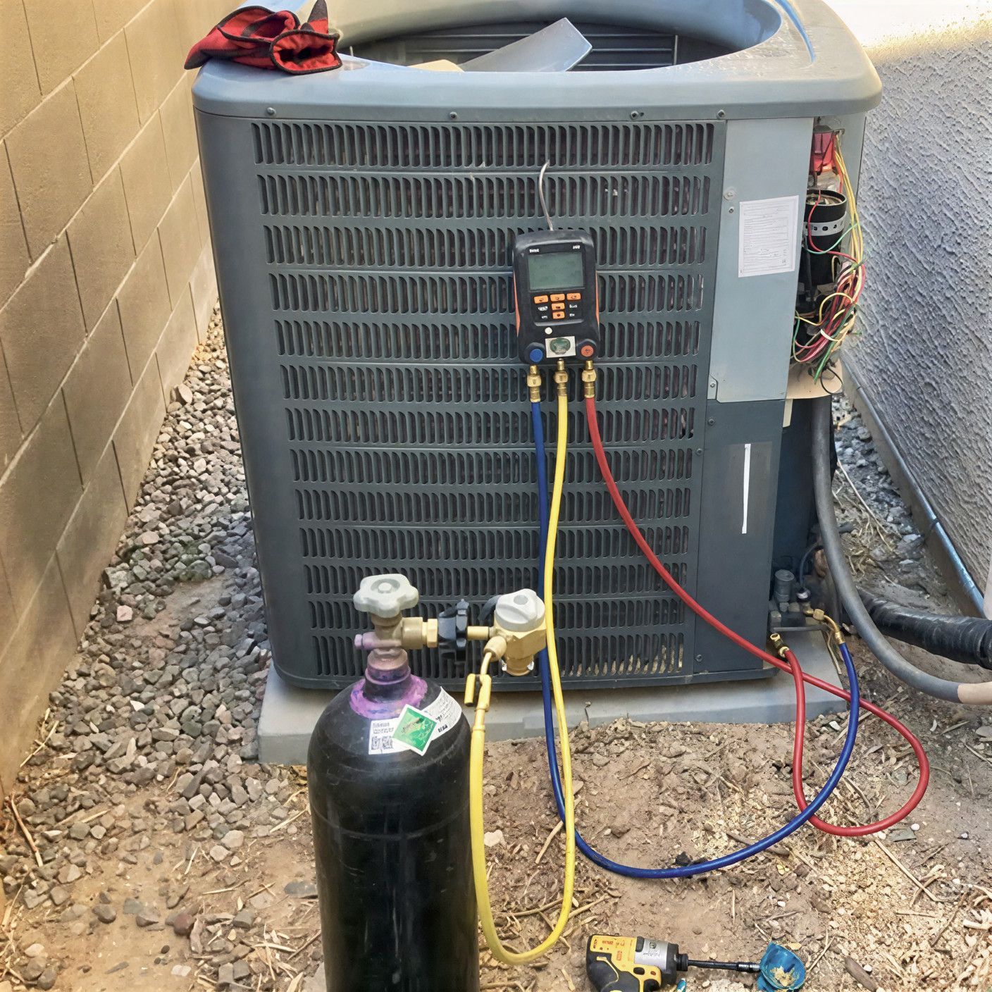 HVAC unit being serviced with gauges and nitrogen tank outdoors.