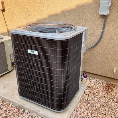 Outdoor air conditioning unit against a beige stucco wall, on a concrete pad with gravel.