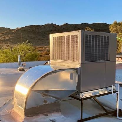 Rooftop HVAC unit with metal ductwork, against a backdrop of mountains under a sunny sky.