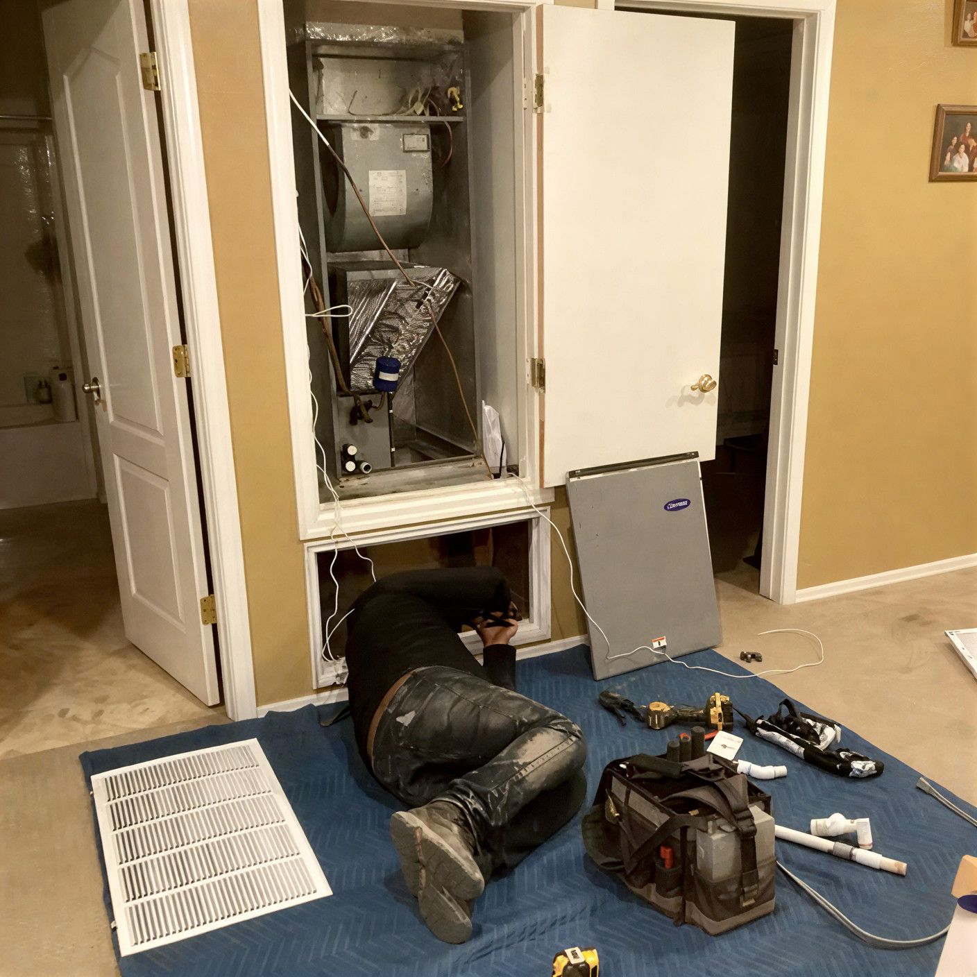 A person working on HVAC system inside a cabinet, tools and parts on floor.