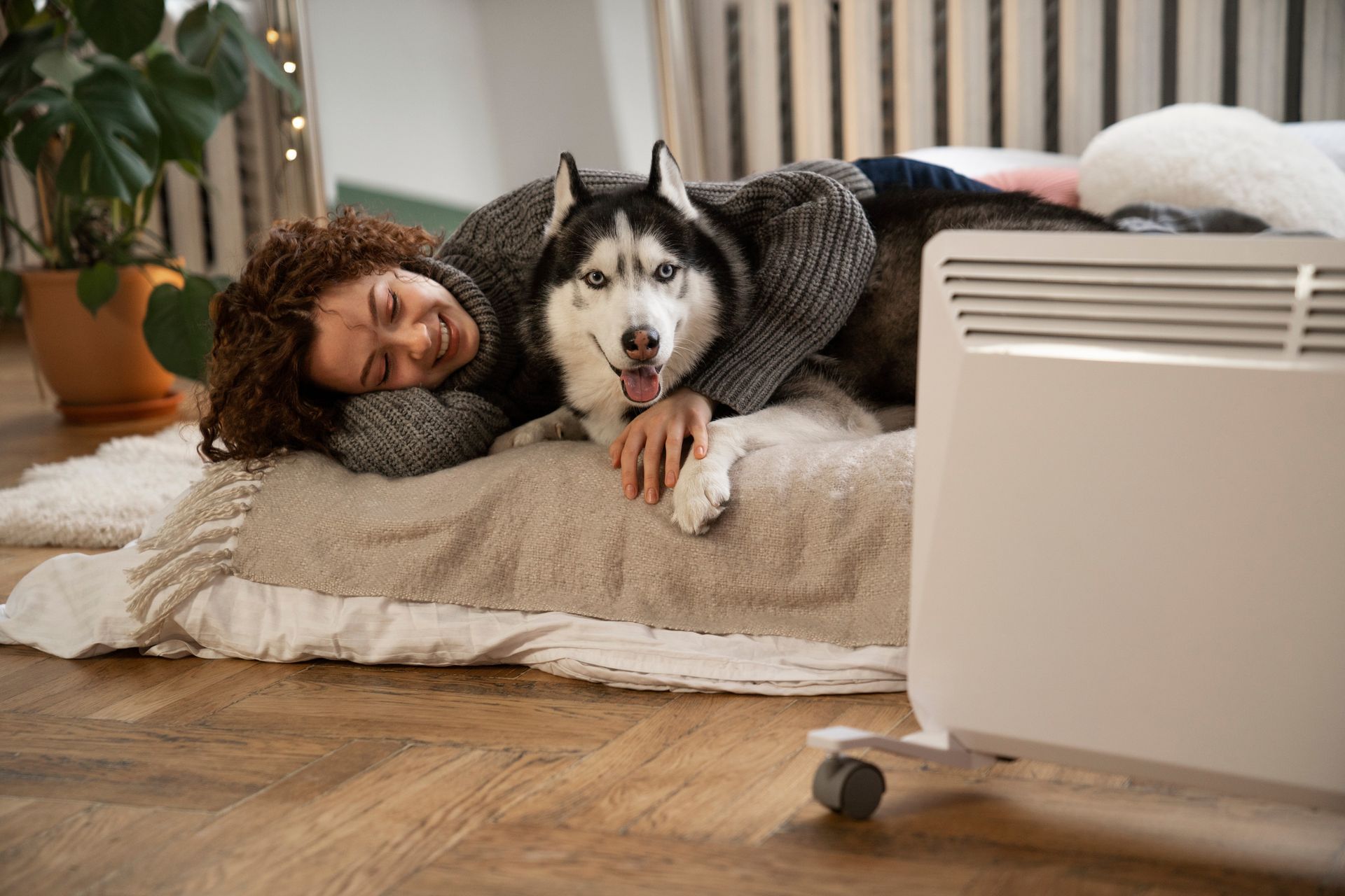 A woman is laying on the floor next to a husky dog.