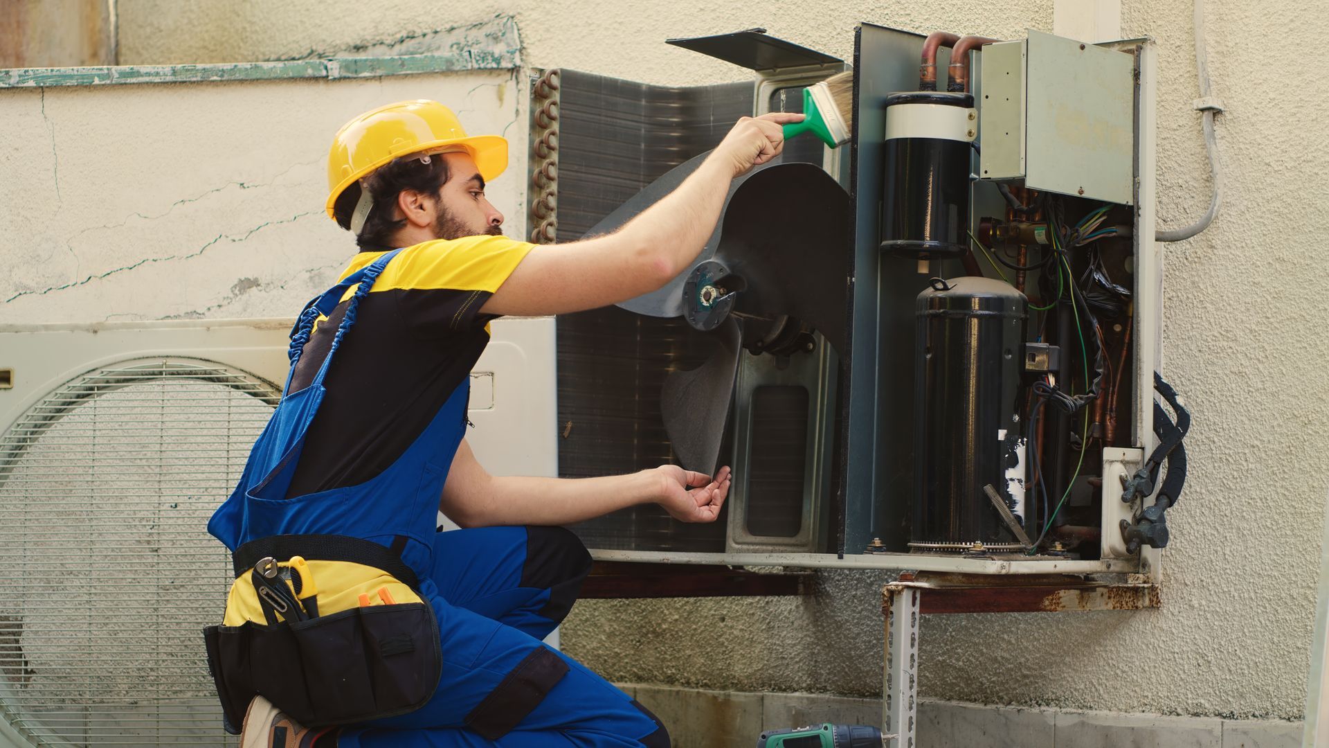 A man is working on an air conditioner outside of a building.
