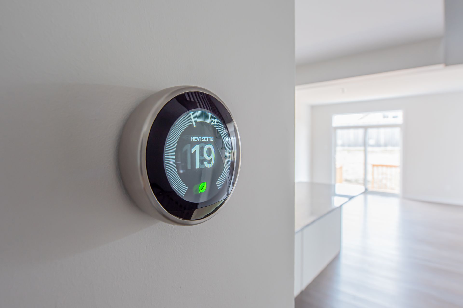 A smart thermostat is hanging on a wall in an empty room.