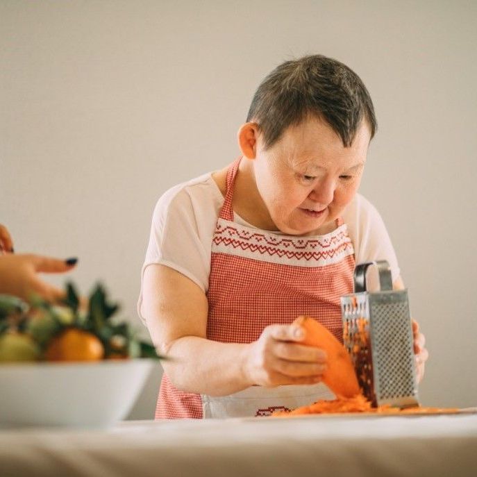 Grating carrot in the kitchen with assistance.