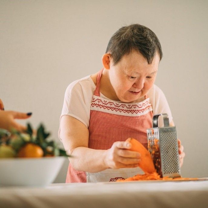 Grating carrot in the kitchen with assistance.