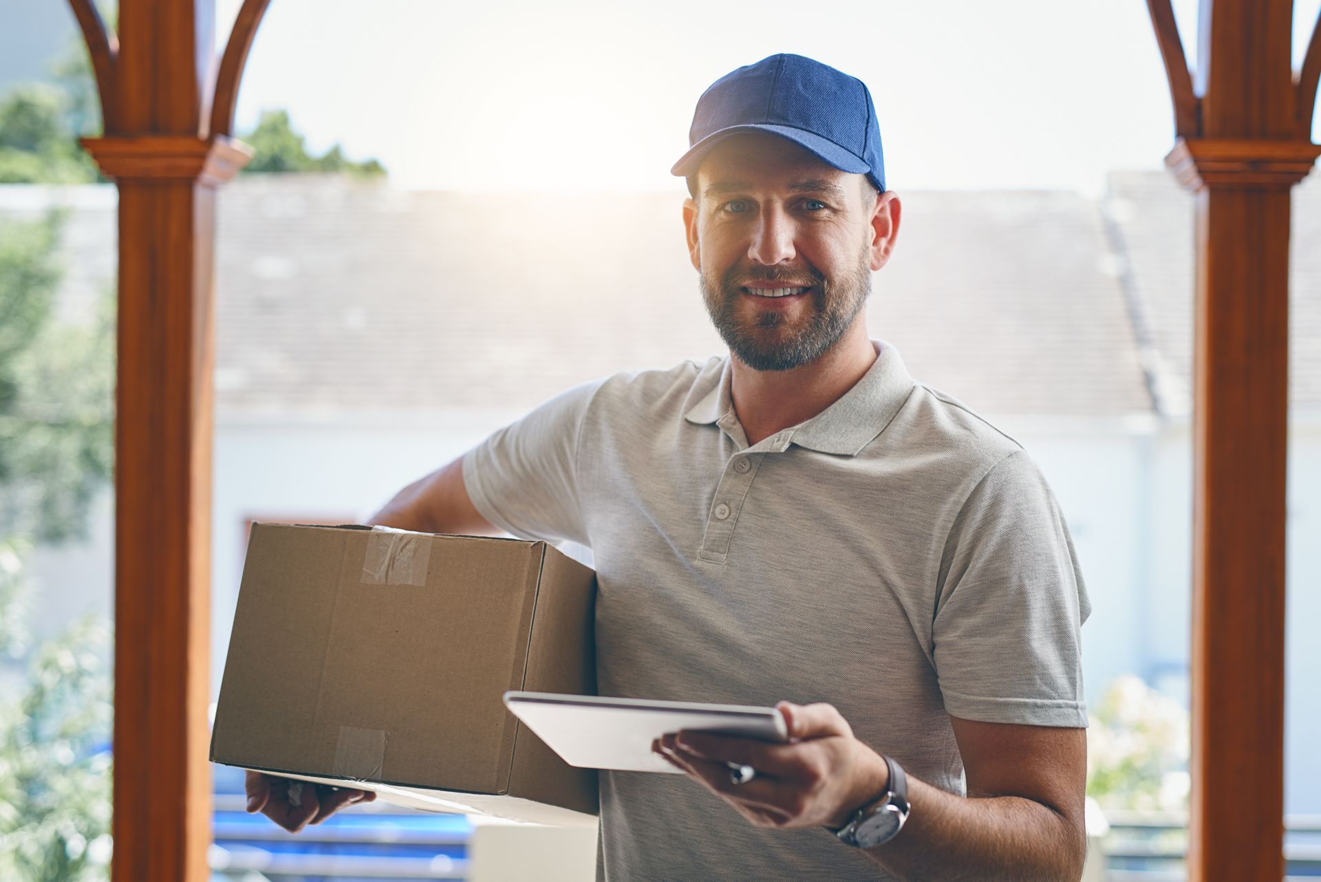 Delivery person holding a package and tablet, smiling at the camera outdoors. Delivery person holding a package and tablet, smiling at the camera outdoors.