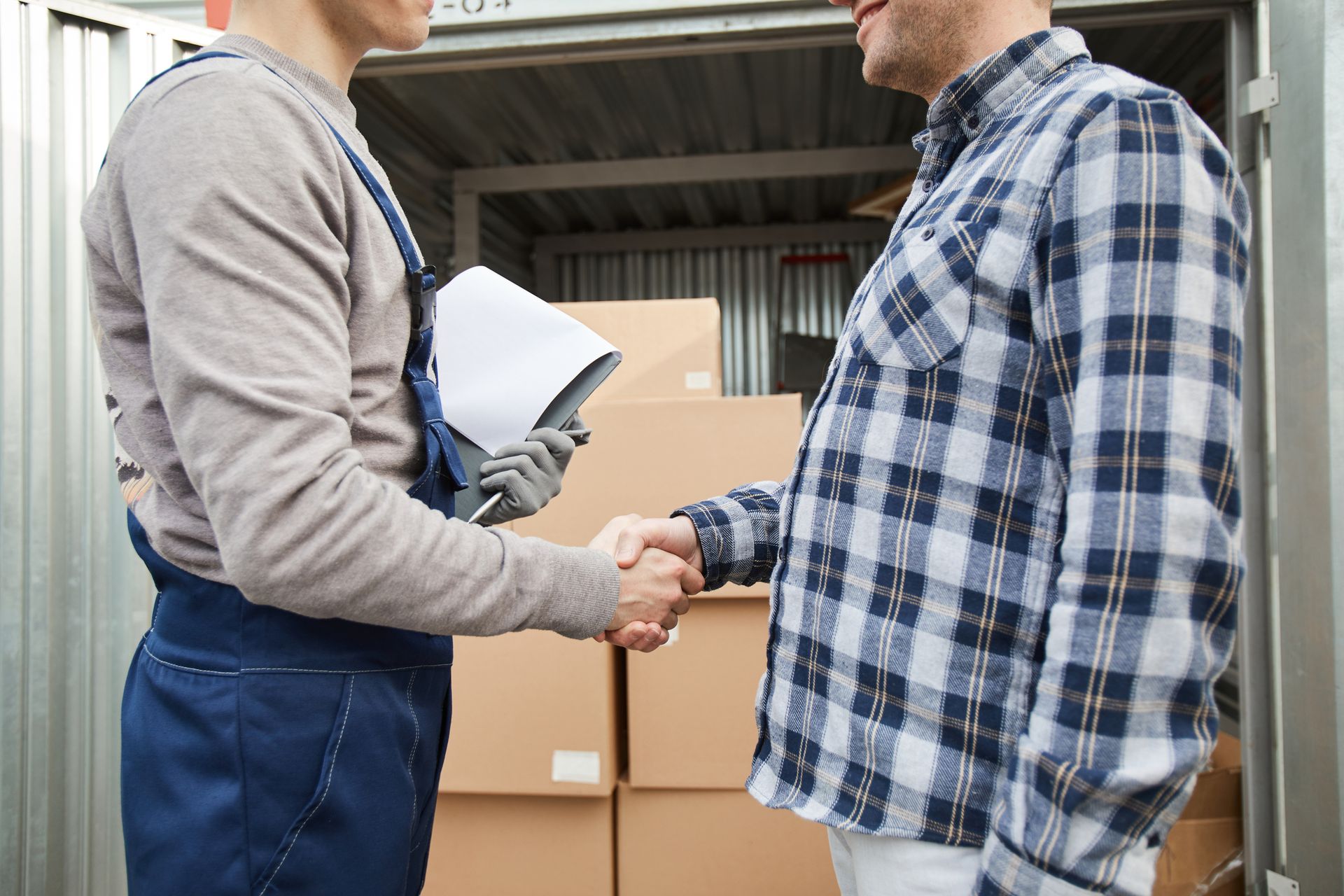Delivery worker shaking hands with customer in storage unit with cardboard boxes.