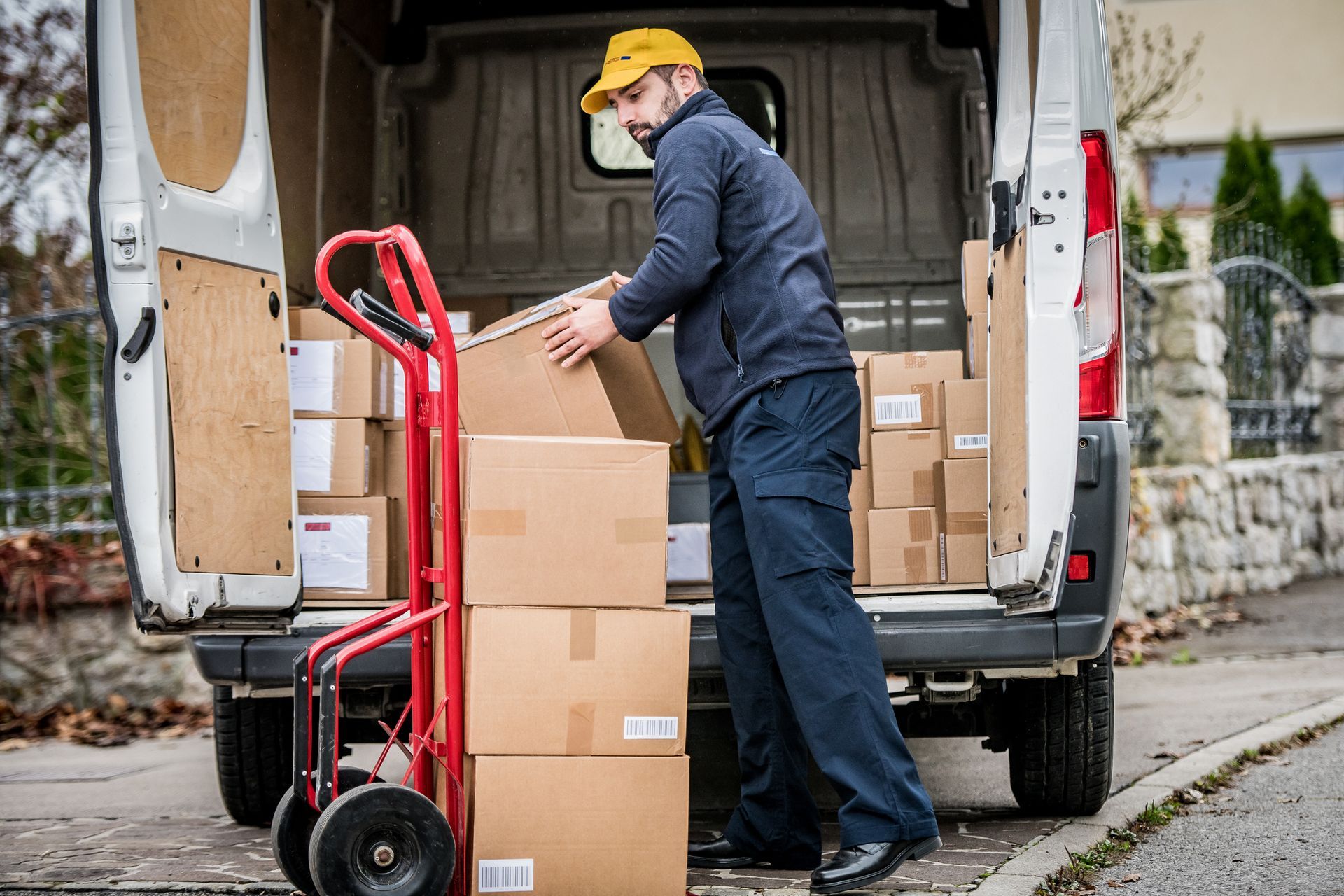 Delivery person loading boxes into a white van from a dolly, on a street. Delivery person loading boxes into a white van from a dolly, on a street.