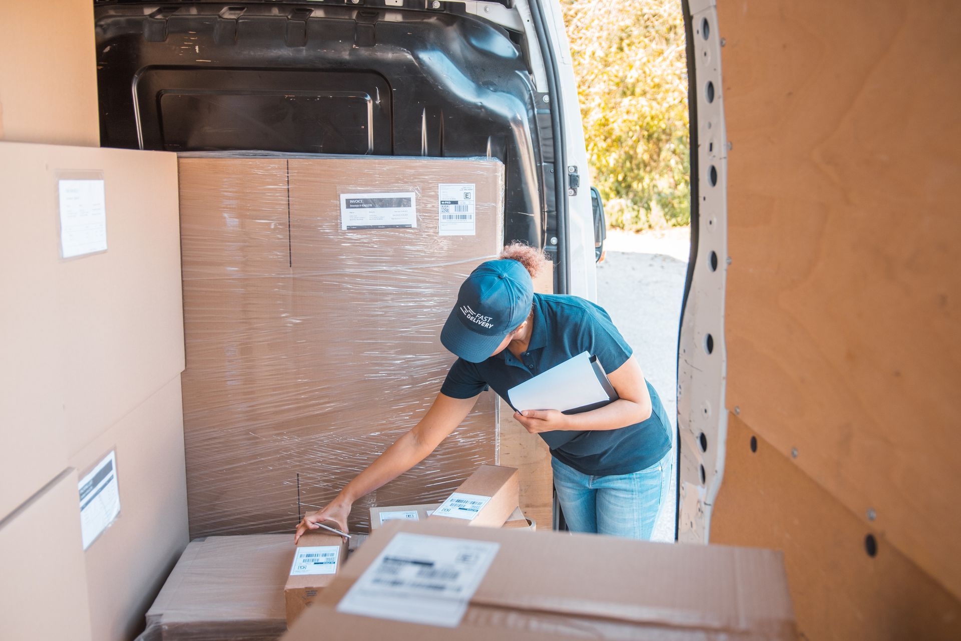 Person in a van, sorting packages. She wears a cap and jeans, checking a clipboard while organizing boxes. Person in a van, sorting packages. She wears a cap and jeans, checking a clipboard while organizing boxes.