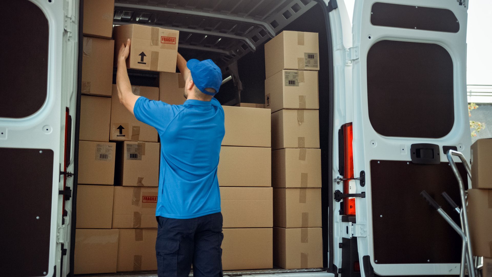 Delivery person stacking boxes inside a white cargo van.