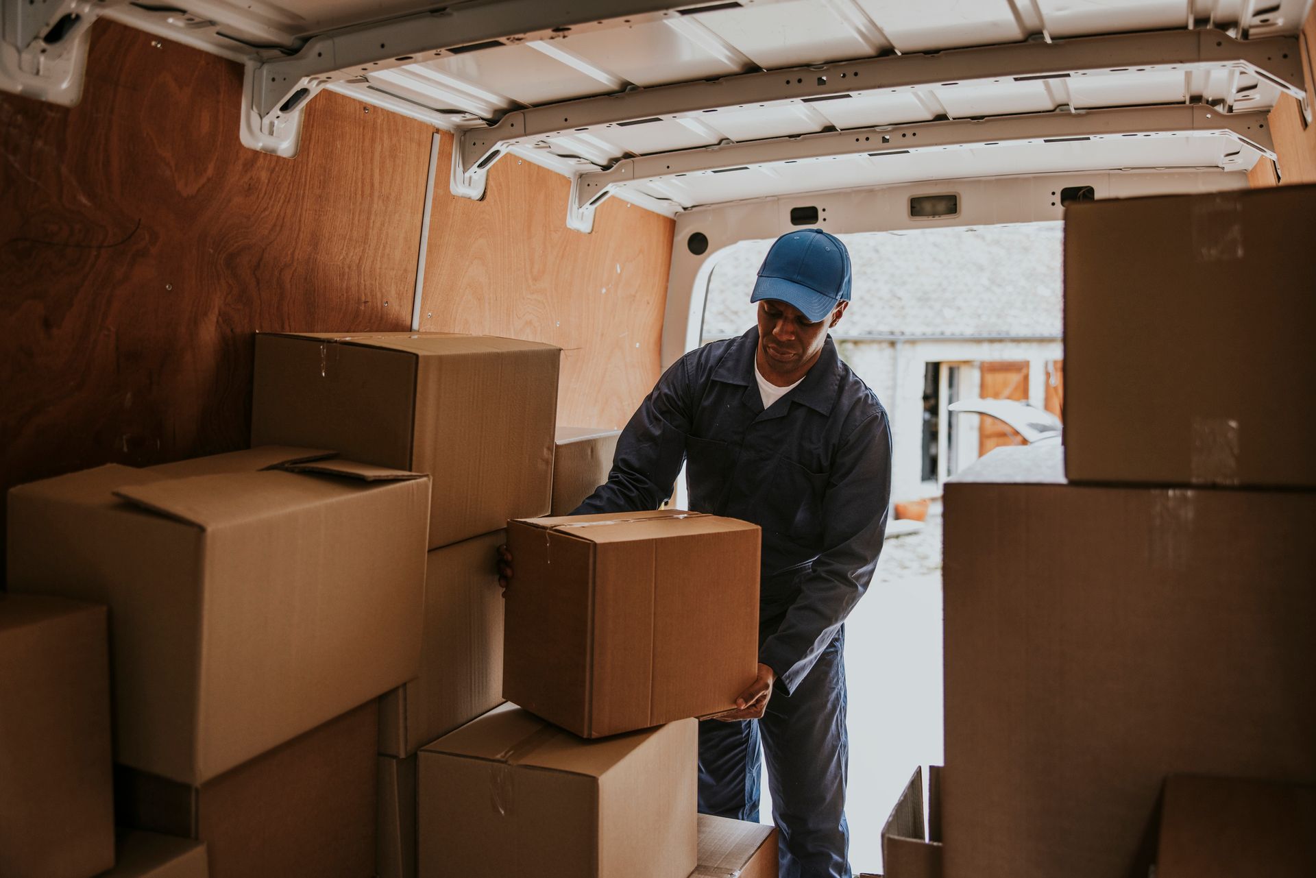 Person in blue uniform inside a van stacking cardboard boxes. Person in blue uniform inside a van stacking cardboard boxes.