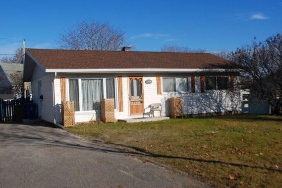 Une petite maison blanche au toit marron se trouve au sommet d'un champ verdoyant.