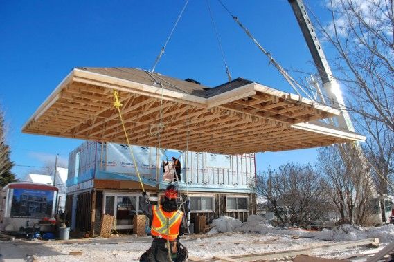 Une grue soulève un gros morceau de bois au-dessus d'une maison en construction.