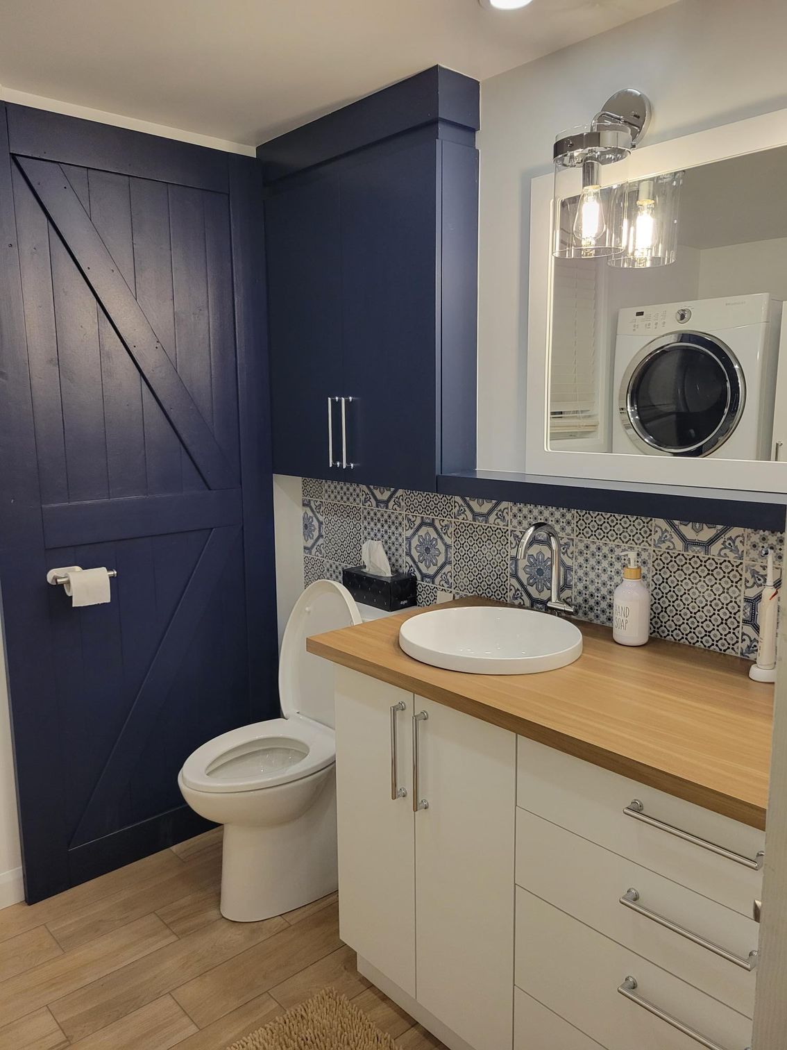 Une salle de bain avec toilettes, lavabo, laveuse et sécheuse.