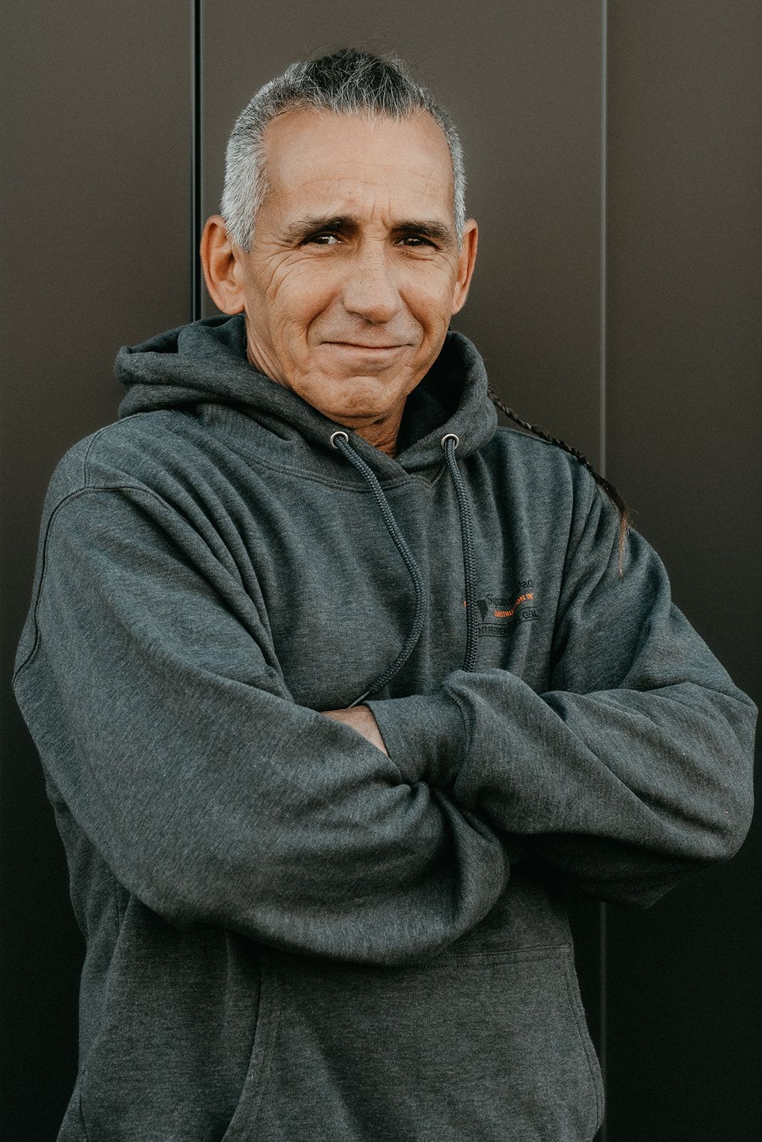 Un homme vêtu d'un sweat à capuche gris est debout, les bras croisés.