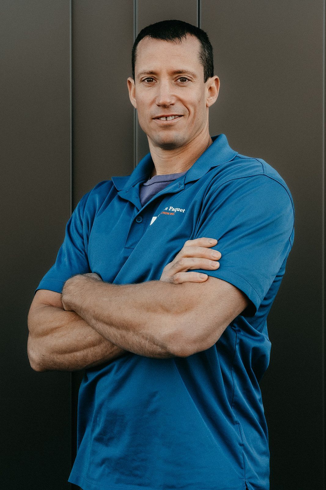 Un homme en chemise bleue est debout, les bras croisés.