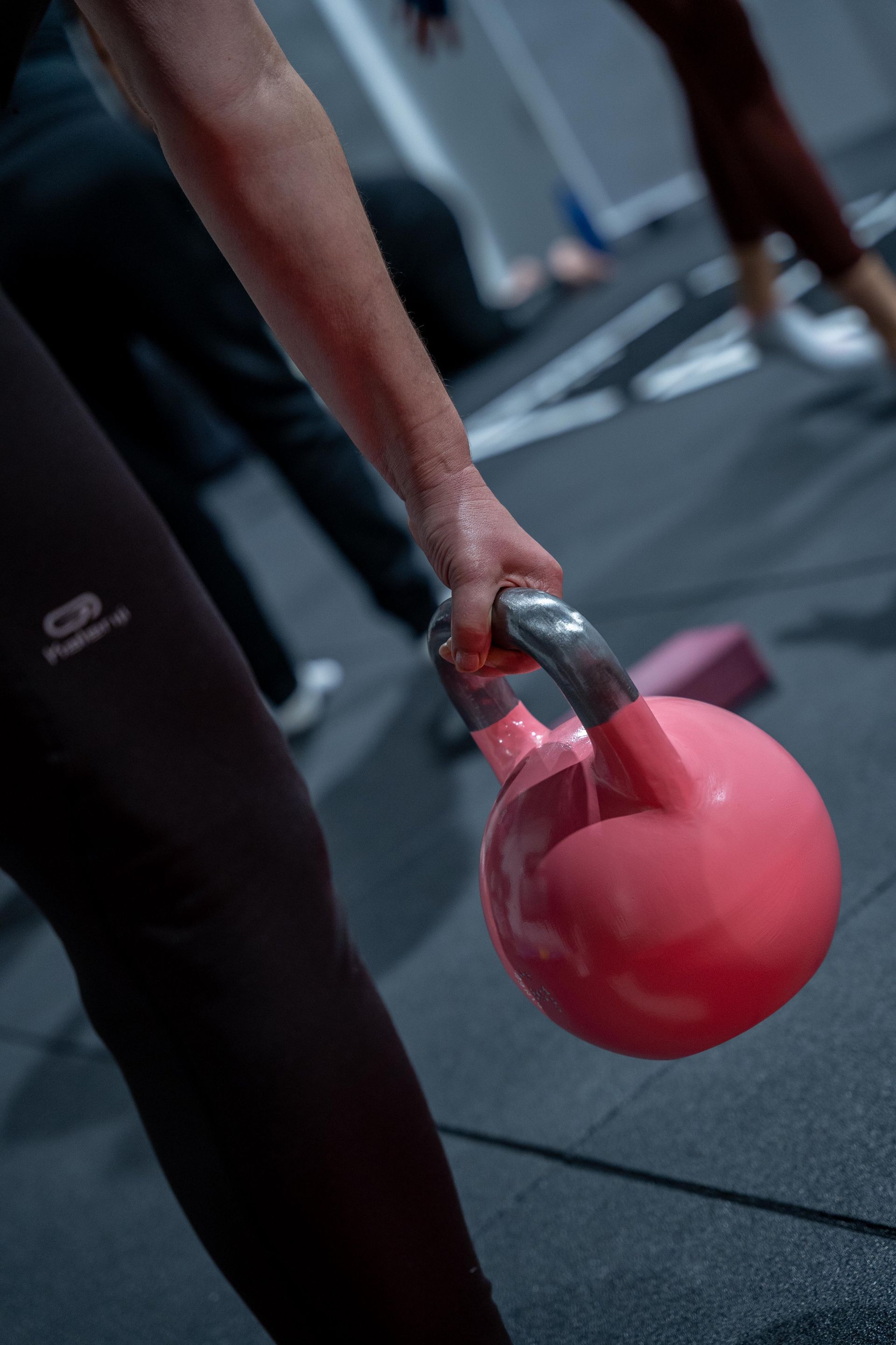 Persona sosteniendo una pesa rusa rosa, probablemente en una clase de fitness.