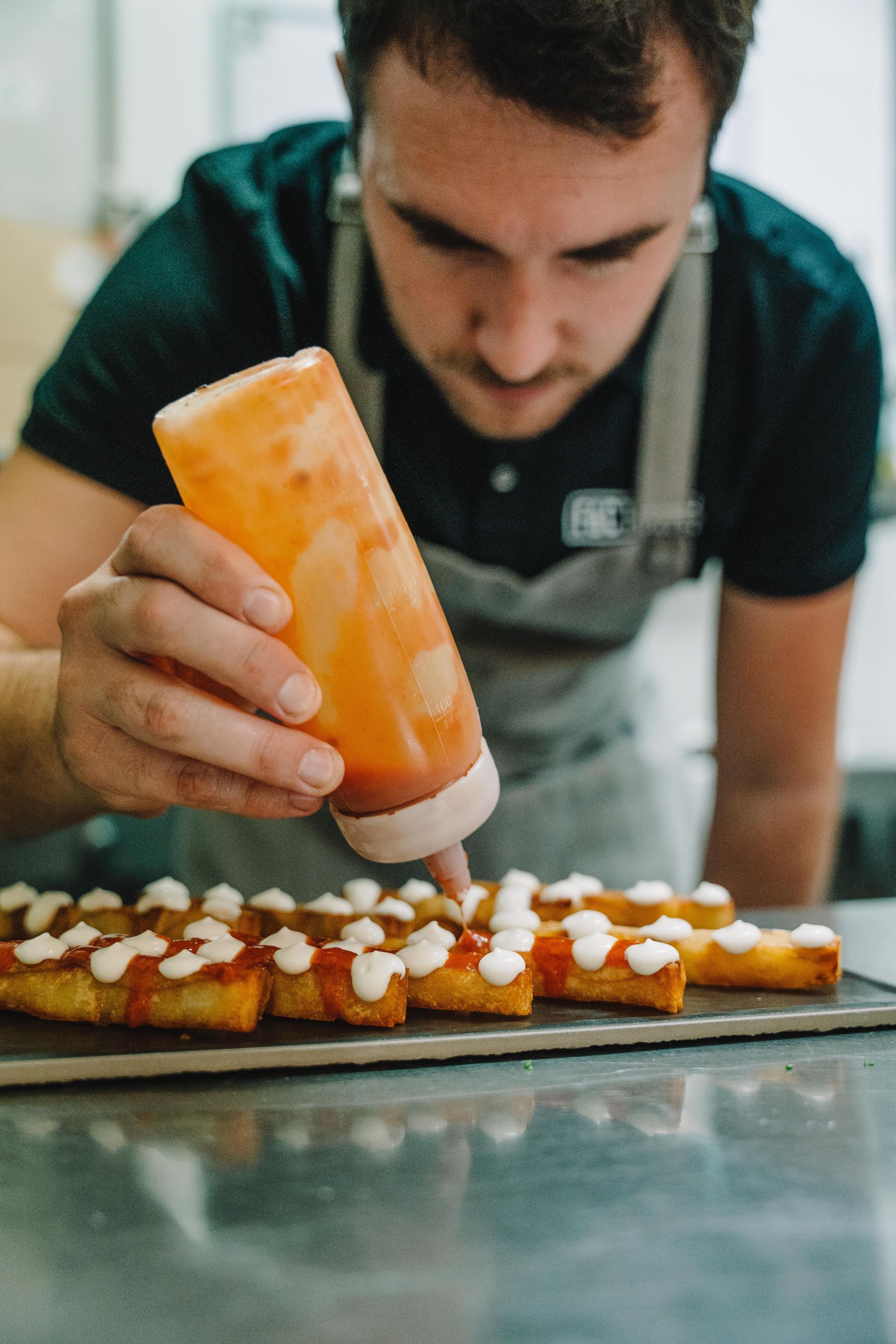 El chef exprime la salsa de una botella sobre los aperitivos alineados en una bandeja oscura.