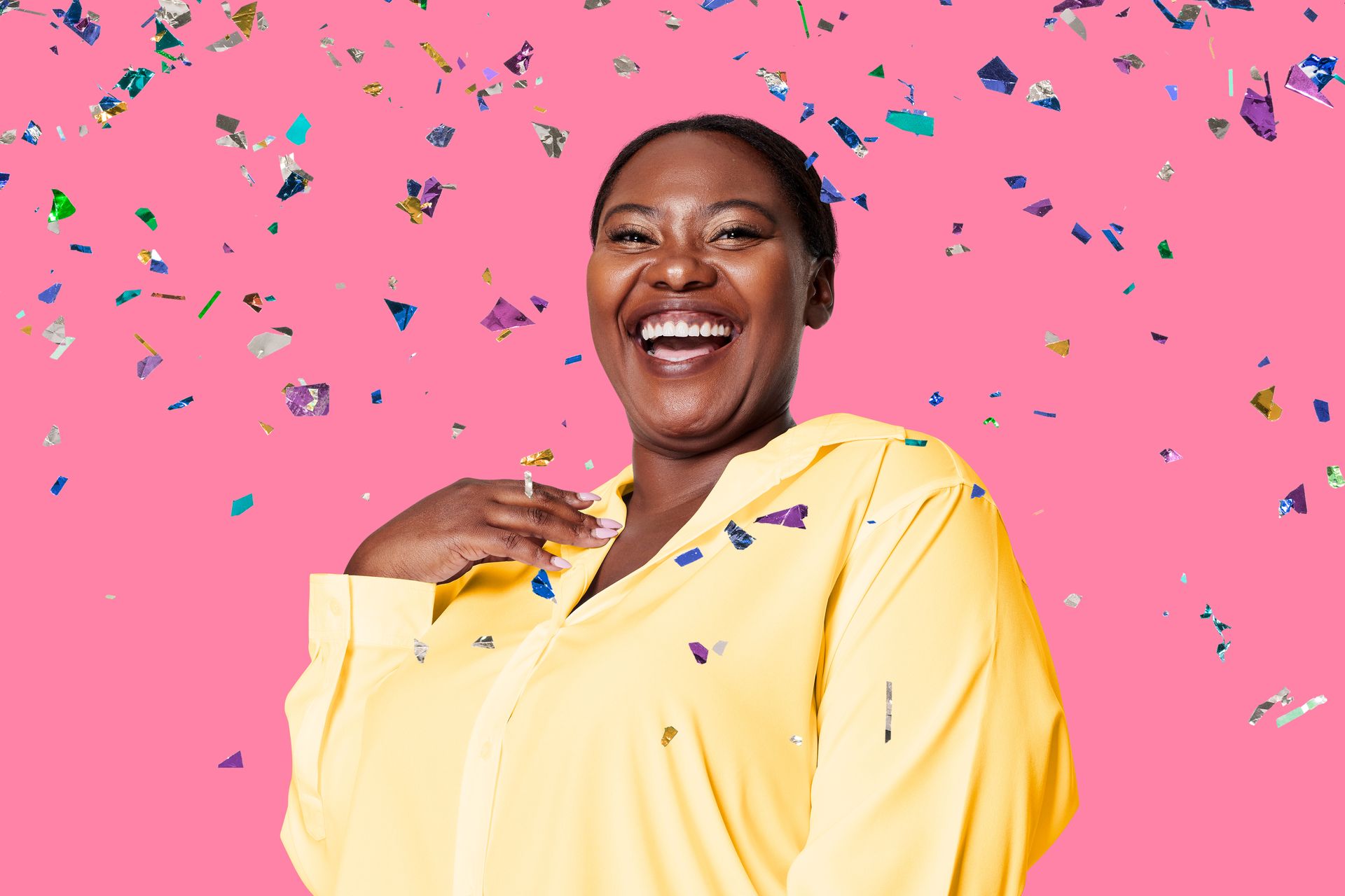 A woman in a yellow shirt is laughing with confetti falling around her.