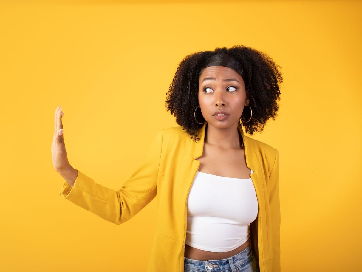 A woman in a yellow jacket is making a stop sign with her hand.