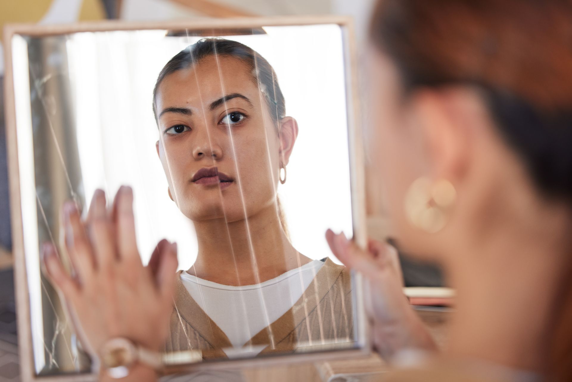 Woman looking in a cracked mirror, touching the cracks with her hands.