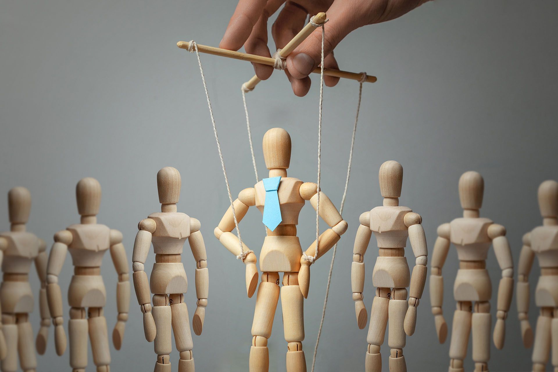 A group of wooden mannequins are being manipulated by a hand.