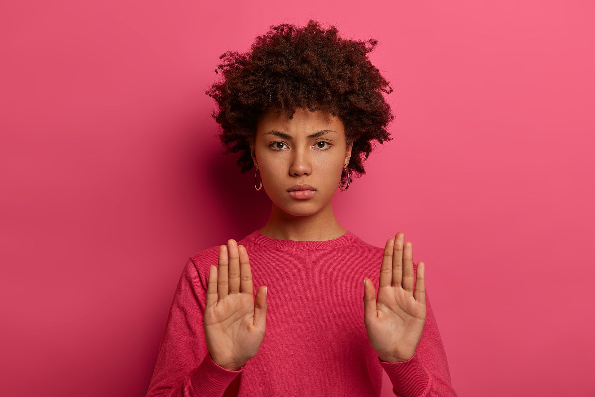A woman in a pink sweater is making a stop sign with her hands.