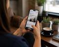 Person browsing a smartphone while reclining on a sofa, with a photo grid visible on the screen