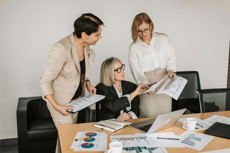 Three professionals in business attire collaborating over documents and charts on a desk in an office.