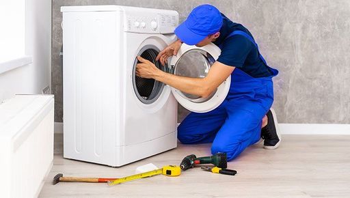 A man is fixing a washing machine in a room.