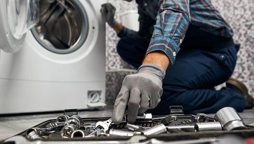 A man is kneeling on the floor fixing a washing machine.