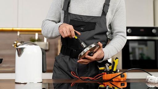 A man is repairing an electric kettle in a kitchen.