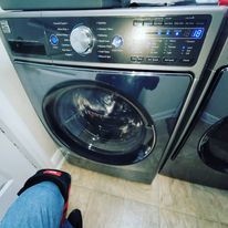 A person is standing next to a washing machine in a laundry room.