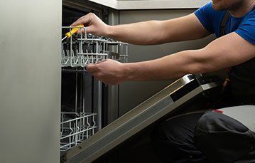 A man is fixing a dishwasher with a screwdriver.