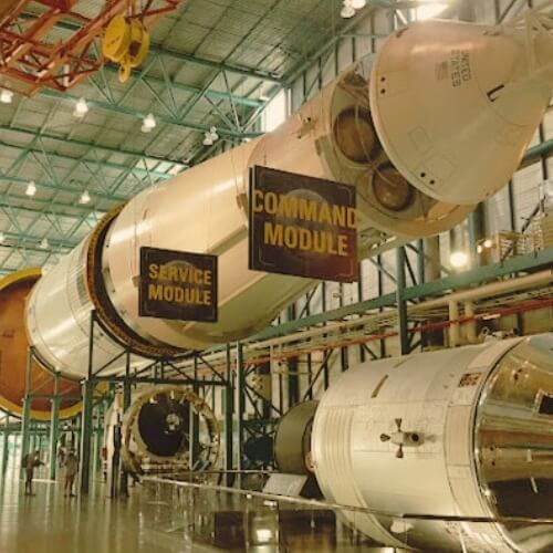 A command module and service module hang from the ceiling of a building