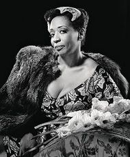 Woman in elegant dress and fur, seated, holding flowers; black and white portrait.