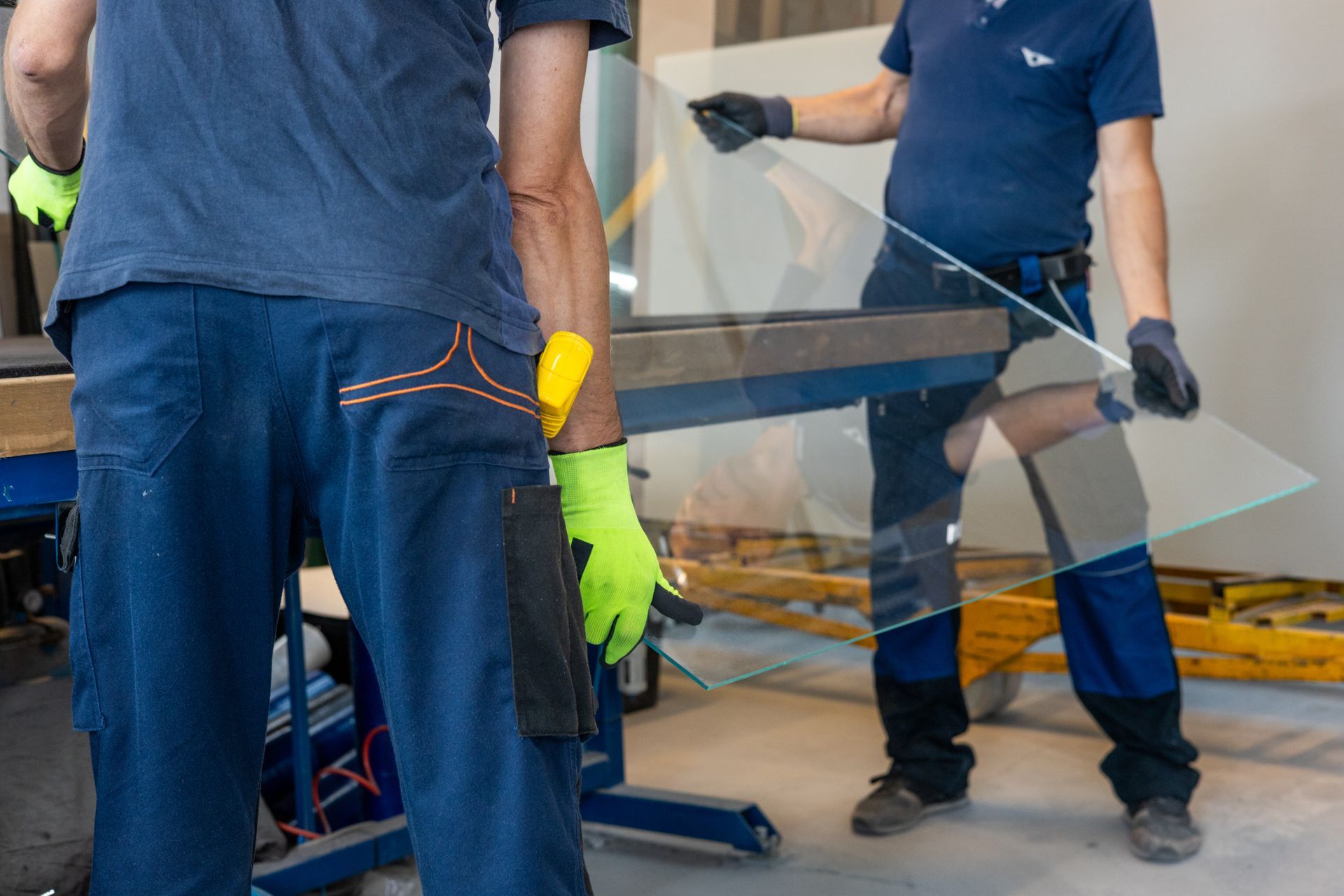 Glaziers place a large pane of glass on a table in a glassworks workshop. Glaziers place a large pane of glass on a table in a glassworks workshop.