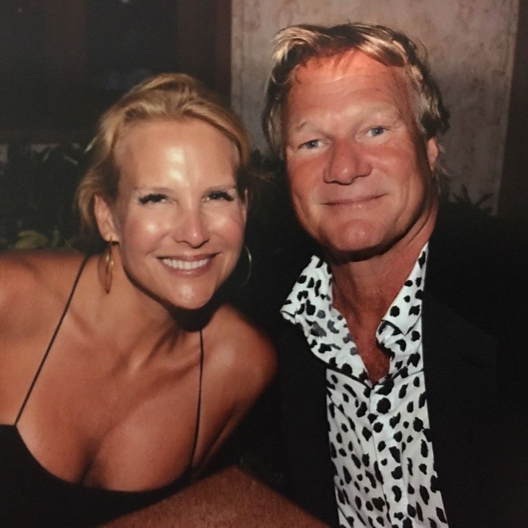 Woman and man smiling, close-up photo. Woman in black top, man in spotted shirt and blazer, night setting.