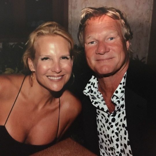 Woman and man smiling, close-up photo. Woman in black top, man in spotted shirt and blazer, night setting.