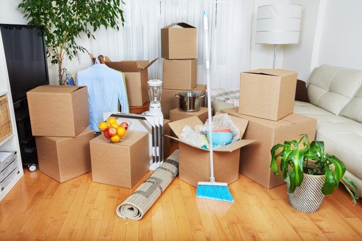 Living room with moving boxes, packed items, and cleaning tools on a wood floor
